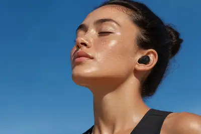 Serene close-up of a freckled woman with earbuds against blue sky