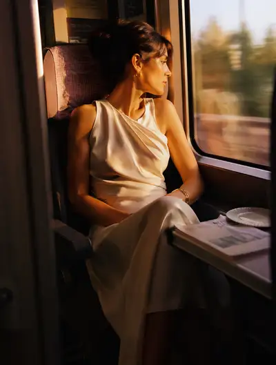 Woman by a train window at golden hour, cinematic fashion still
