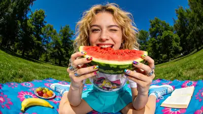 Fisheye lens photo of a woman biting into watermelon at a picnic