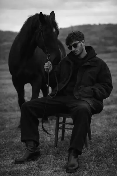 Stoic black and white portrait of a man with a horse in an open field