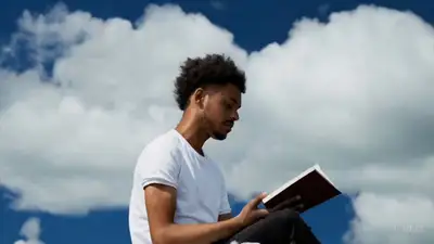 Young man on a cloud reading a book