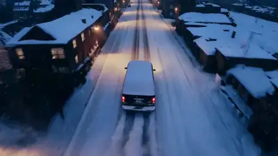 High Rear-Facing Aerial Shot of Black GMC Van on Snowy Road