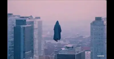Aerial View of Cloaked Figure Rising Between Skyscrapers