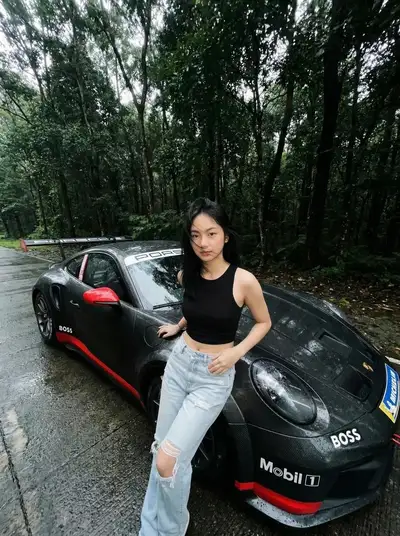 Femme cinématographique près d'une Porsche noire mouillée sur une route forestière