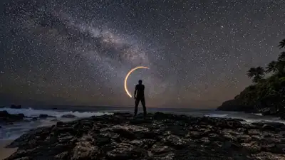 Silueta pintando con luz un círculo brillante en una playa estrellada