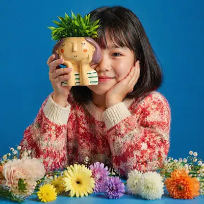 Cute girl portrait with a planter and winter sweater on blue backdrop