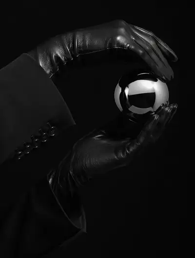 Editorial close-up of leather gloves holding a chrome sphere